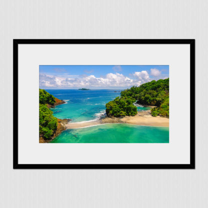 Aerial view of clear blue colored water at the edge of a white sand beach with jungle island plants