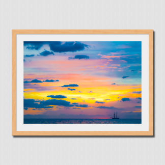 Distant schooner ship with colorful spectrum sky and cloud formations